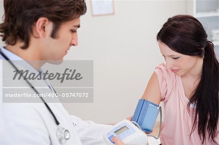 Young male doctor taking female patients blood pressure