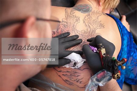 Male tattoo artist draws a design on back of client