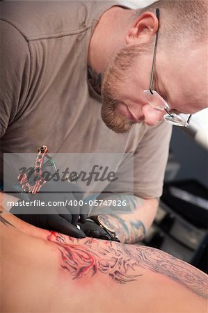 Caucasian tattoo artist inks a design on customer's back