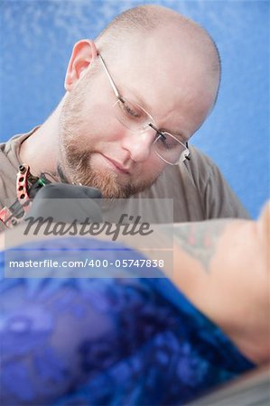 Bald Caucasian tattoo artist makes a design on client's back