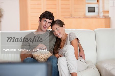 Young couple with bowl on popcorn watching a movie on the sofa