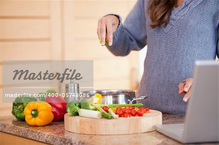 Young woman adding herbs to her vegetable stew