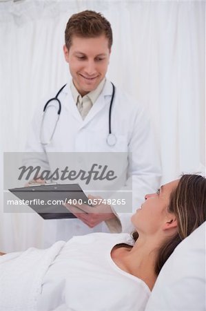 Doctor with clipboard talking with bedridden patient