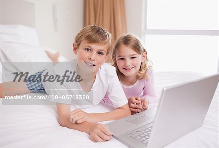 Siblings using a laptop in a bedroom