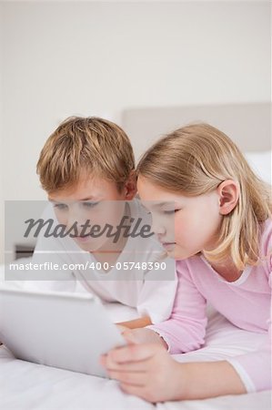 Portrait of cute children using a tablet computer in a bedroom