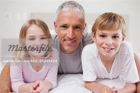 Smiling siblings and their father posing in a bedroom