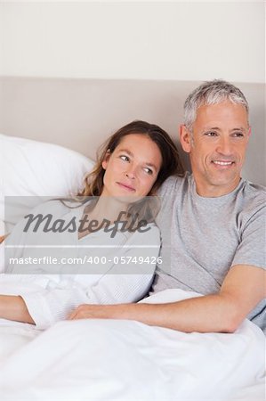 Portrait of a happy couple lying on a bed while looking away from the camera