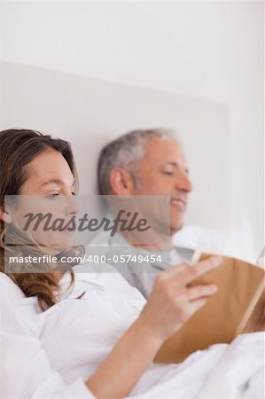 Portrait of a woman reading a book while her husband is reading a newspaper in their bedroom