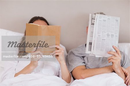 Woman reading a book while her companion is reading a newspaper in their bedroom