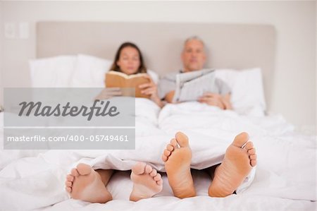 Woman reading a book while her companion is reading the news in their bedroom