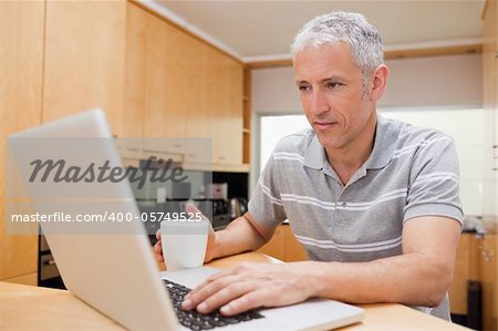Man using a laptop while drinking coffee in a kitchen