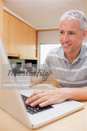 Portrait of a man using a notebook while drinking coffee in a kitchen