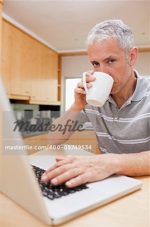 Portrait of a man using a laptop while drinking tea in a kitchen