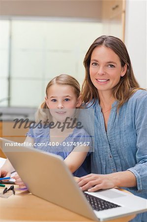 Portrait of a girl doing her homework while her mother is working with laptop in a kitchen
