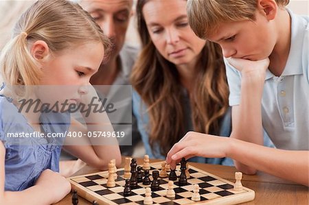 Close up of serious children playing chess in front of their parents in a living room