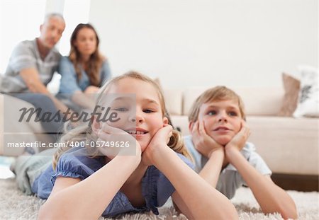 Children lying on a carpet while their parents are sitting on a sofa