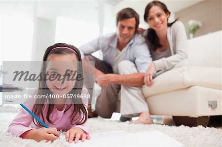 Cute girl drawing with her parents in the background in a living room