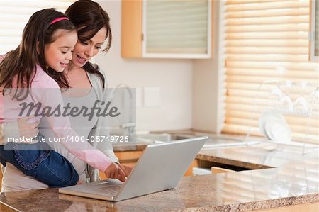 Girl and her mother using a laptop in a kitchen
