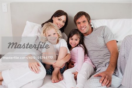 Smiling family posing on a bed while looking at the camera