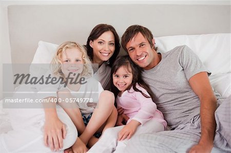 Happy family posing on a bed while looking at the camera