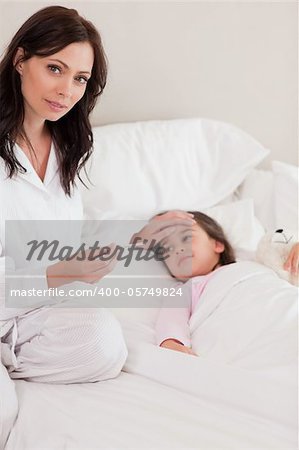Portrait of a concerned mother checking on her daughter's temperature in a bedroom