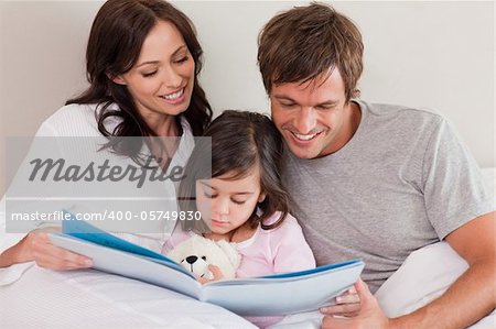 Happy parents reading a story to their daughter in a bedroom