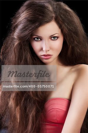 young pretty brunette with hair style wearing an elegant pink dress sitting on a black sofa, she is in foreground and looks in to the lens