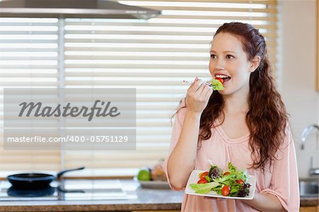 Young girl eating some salad in the kitchen