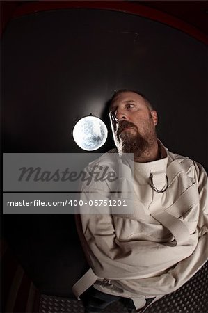 Photo of a insane man in his forties wearing a straitjacket leaning up against an asylum door.  Taken with a fisheye lens.