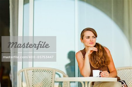 Thoughtful woman sitting on terrace and having cup of coffee