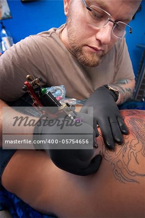 Caucasian Tattoo technician engraves a tattoo on woman's back