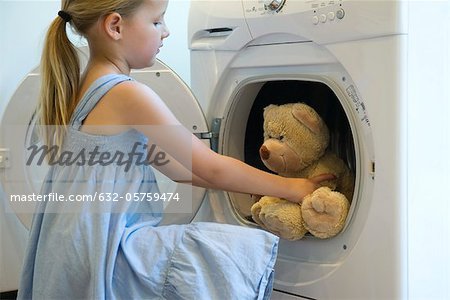 Little girl taking teddy bear out of dryer
