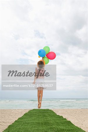 Girl jumping with bunch of balloons, reaching for sky, rear view