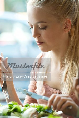 Junge blonde Frau mit Messer und Gabel essen