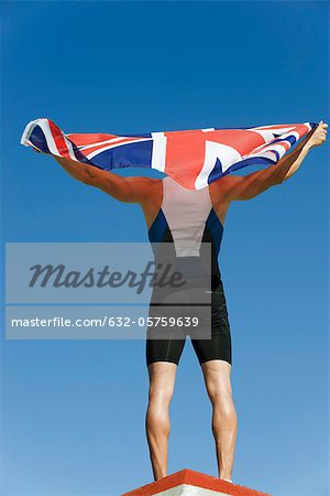 Athlète masculin sur le podium, brandissant le drapeau britannique, vue arrière