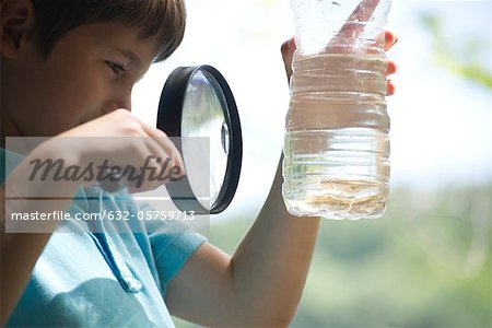 Boy looking at fish in water bottle with magnifying glass