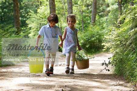 Children walking hand in hand in woods, carrying basket and bucket