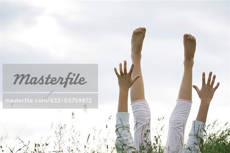 Girl lying on back in tall grass with arms and legs raised in the air