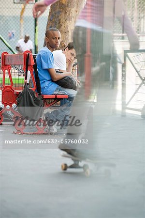 Young men sitting on bench watching person skateboarding
