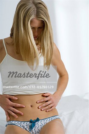 Woman sitting on bed, looking down at abdomen