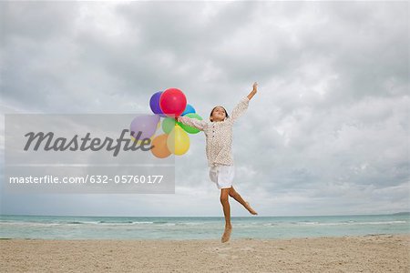 Girl jumping on beach with bunch of colorful balloons