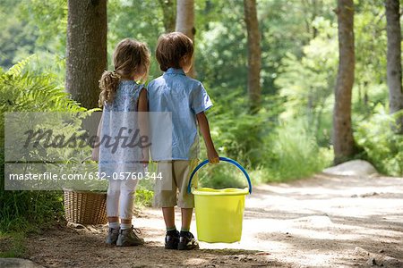 Children together on path in woods, girl carry basket and boy carrying bucket