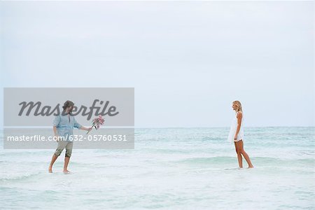 Couple walking on water towards each other, man holding out bouquet