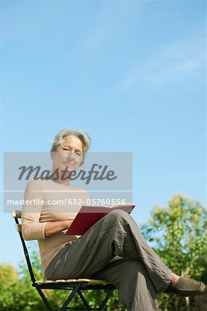 Senior woman sitting outdoors with book, portrait