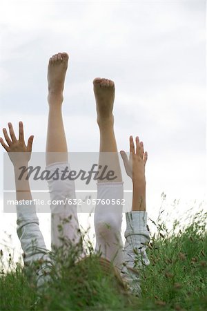 Girl lying on back in tall grass with arms and legs raised in the air