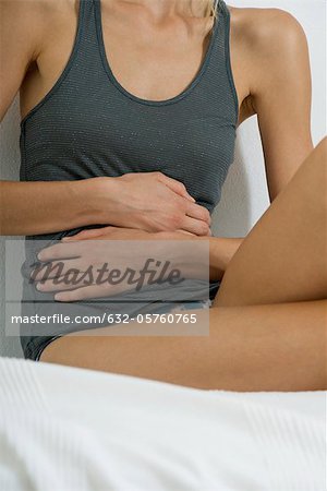 Woman sitting on bed, hands on stomach, mid section