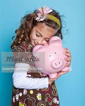 Girl (8-9) embracing piggybank, studio shot