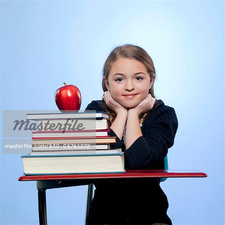 Studio portrait of girl (10-11) with stack of books and apple