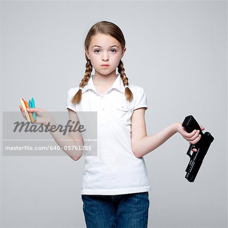 Studio shot of girl (10-11) holding handgun and crayons