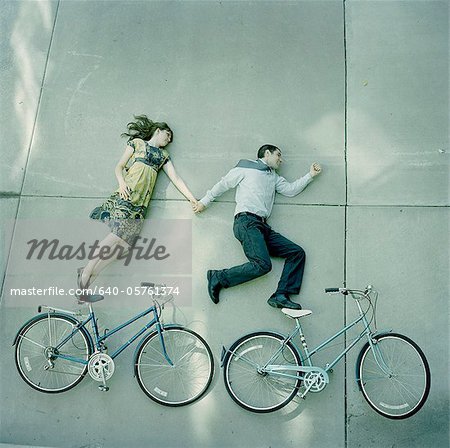 USA, Utah, Salt Lake City, Couple lying holding hands and lying on pavements with their bikes